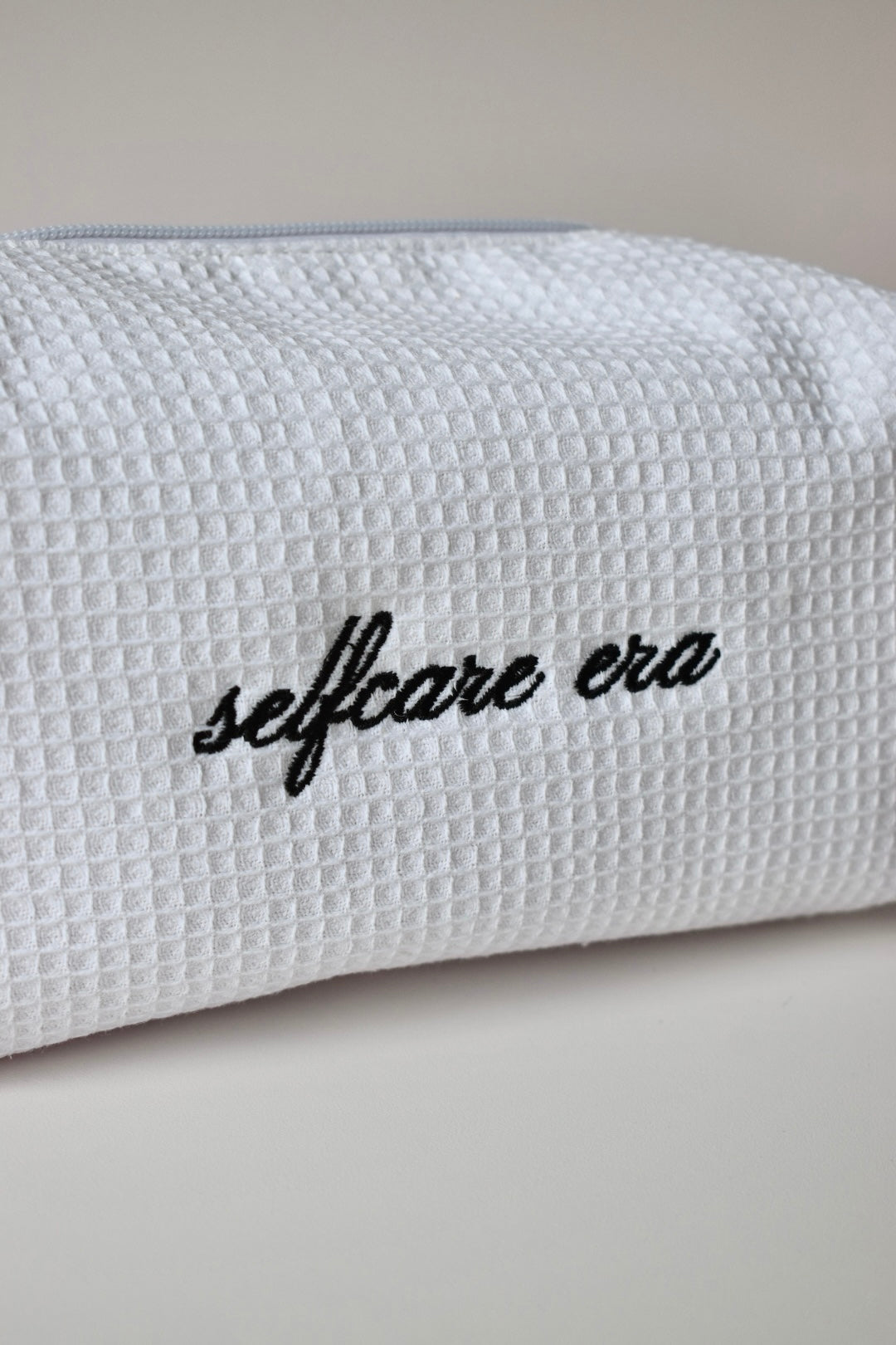 Detail van wit wafelstof make-up tasje met stijlvolle borduring ‘selfcare era’, een musthave voor je selfcare routine.